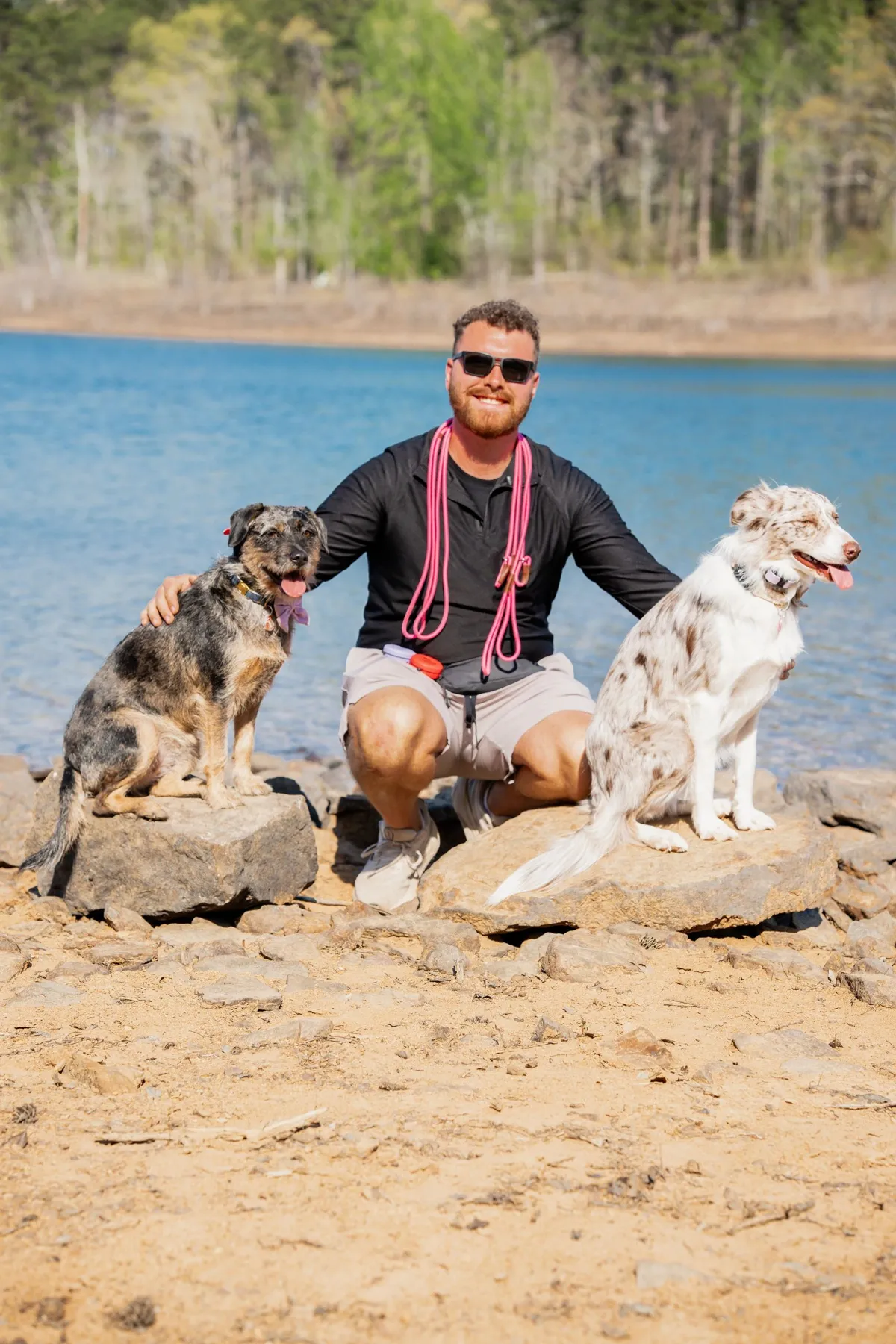 Seth Purdom kneeling between two Australian shepherds at the lake